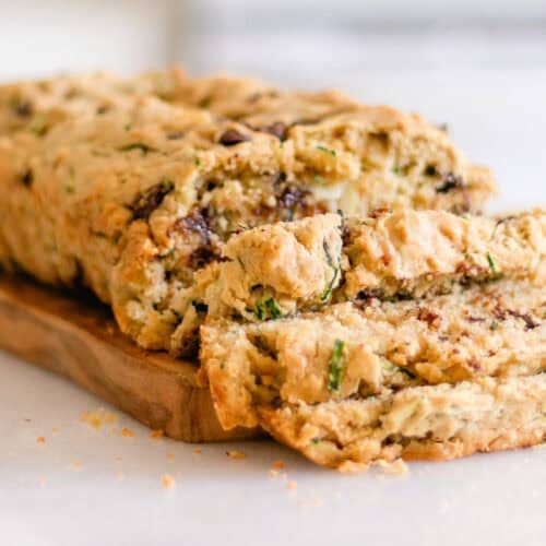 A loaf of gluten-free zucchini bread sliced on a wooden board.
