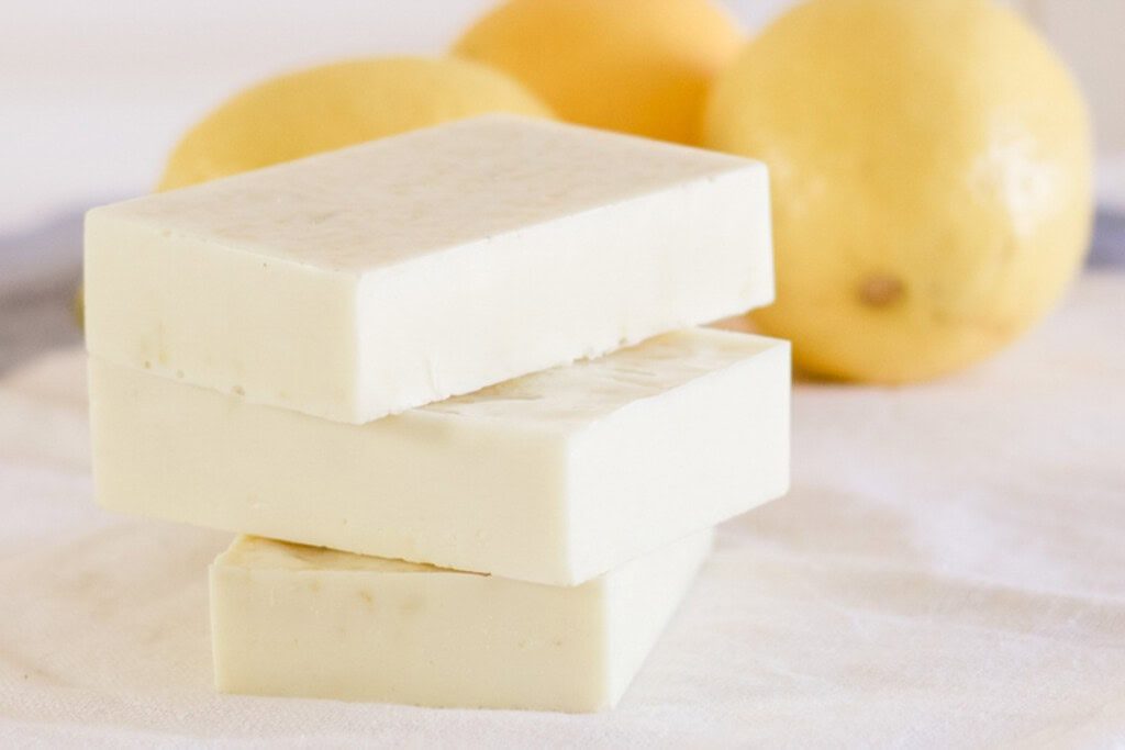 Yellow goat milk soap bars stacked by some fresh lemons.