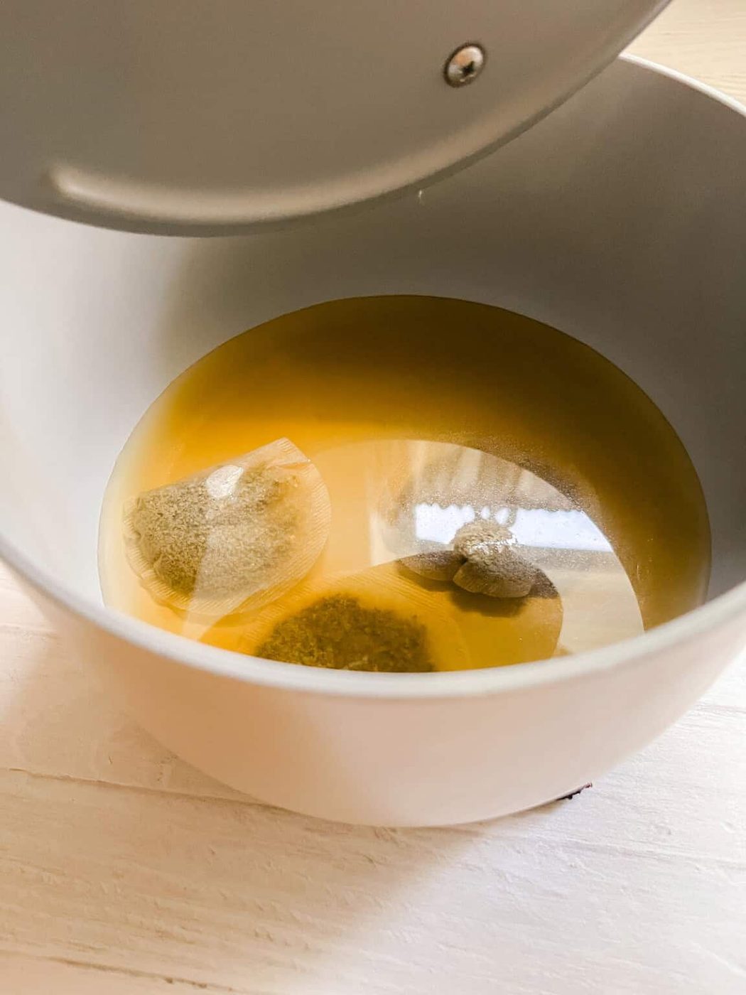 Green tea bags steeping in a saucepan of water.