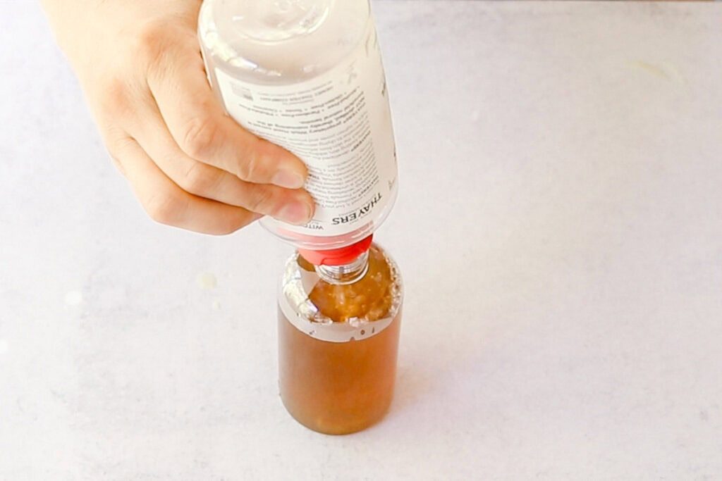 Pouring witch hazel into a bottle of tea.