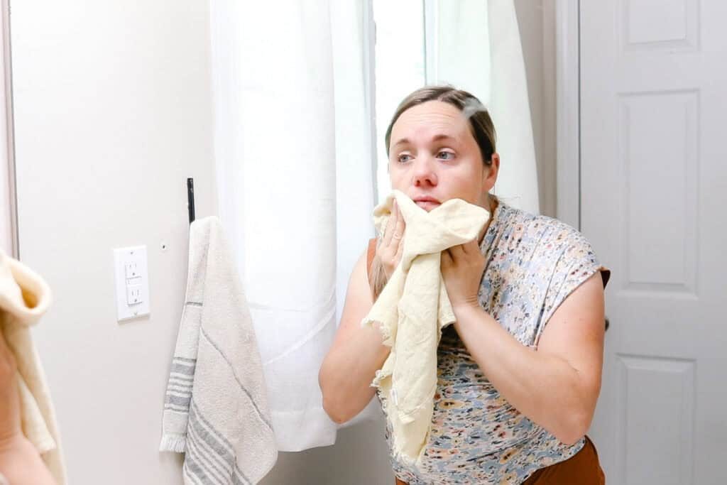 the studio patting her face dry with a towel after cleansing it in a bathroom mirror.