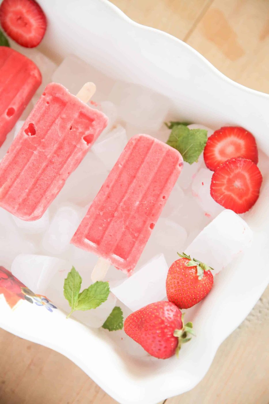 red popsicles strawberry slices and peppermint leaves on ice