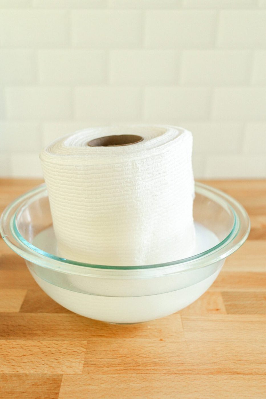 A roll of paper towels sitting in a bowl of baby wipe solution and soaking it up.