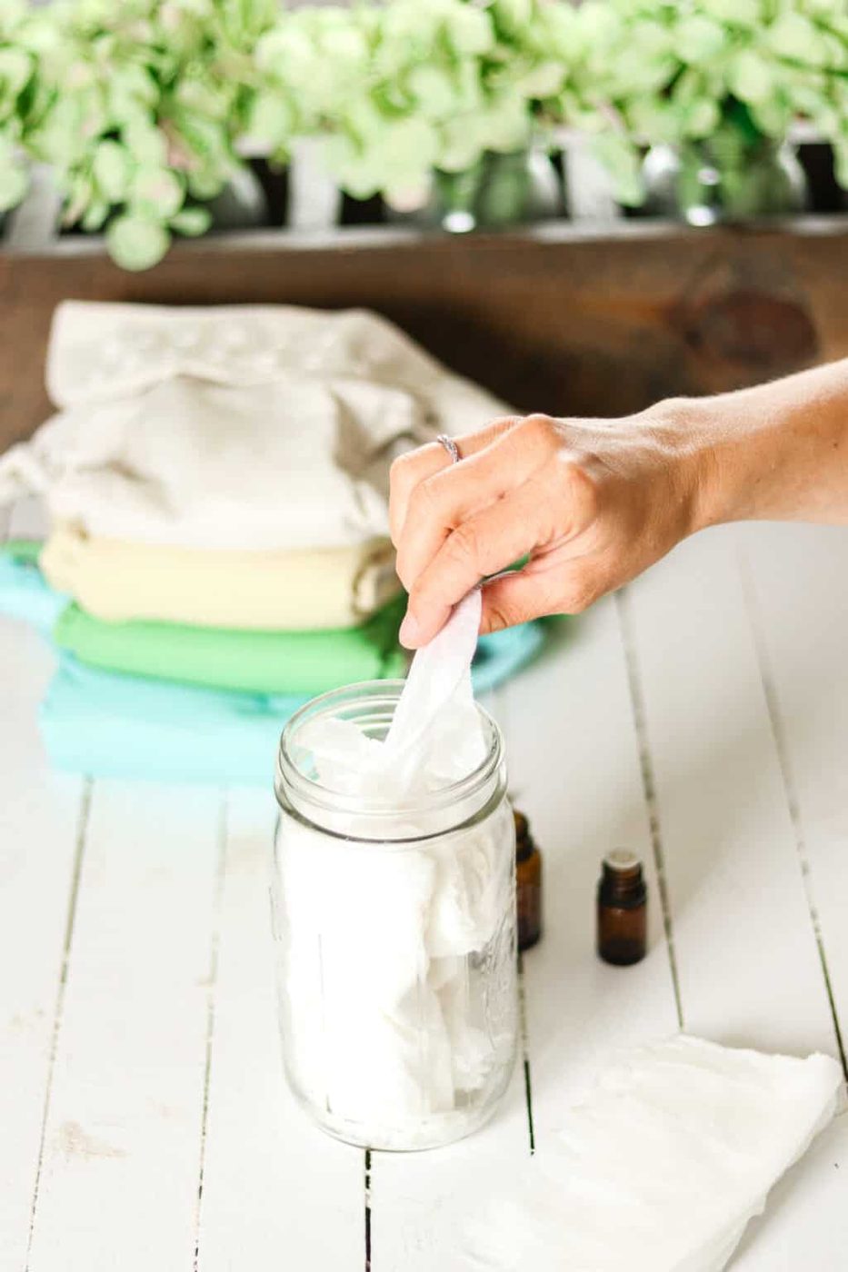 Pulling a homemade natural baby wipe out of a mason jar next to a cloth diaper.
