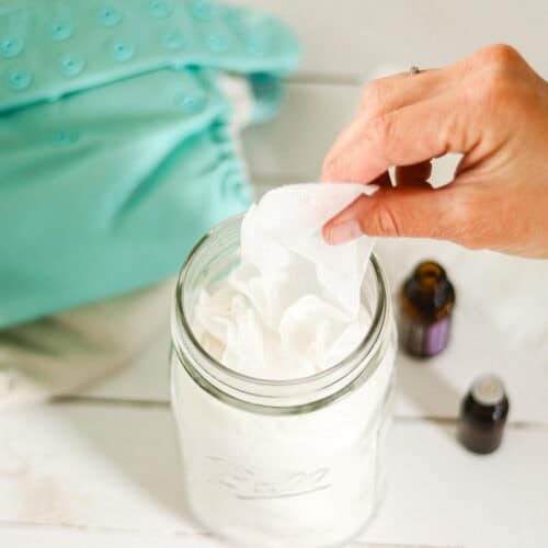Pulling a homemade natural baby wipe out of a mason jar next to a cloth diaper.