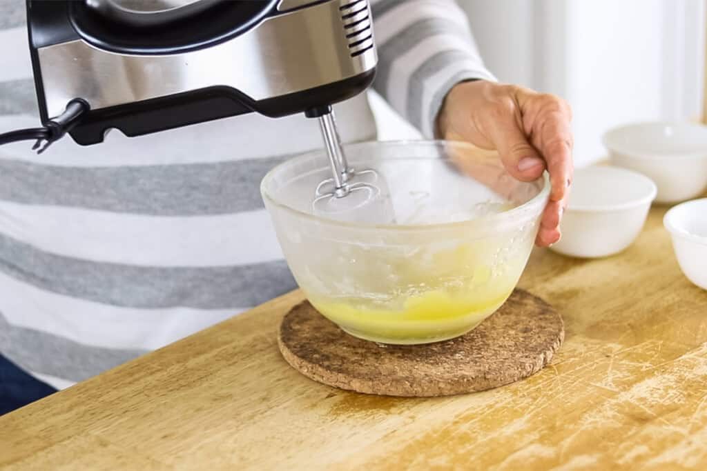 Whipping beard conditioning balm with a hand mixer in a glass bowl.