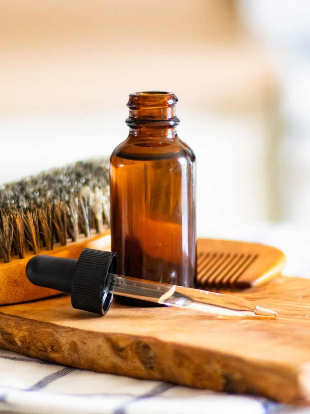 An open bottle of homemade beard oil on a wooden board with a beard brush in the background.