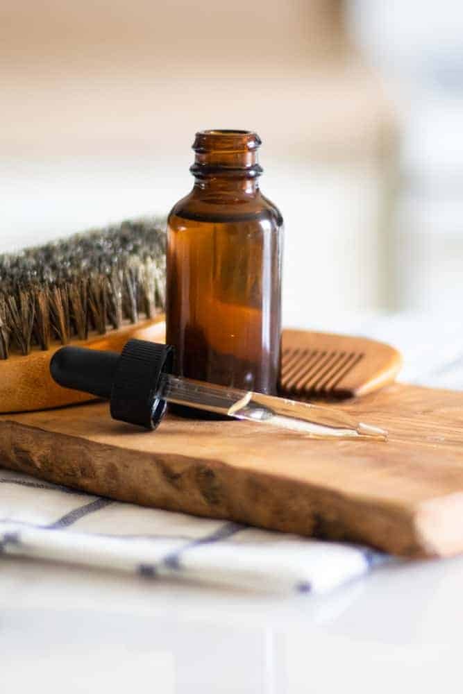 Dropper bottle with essential oils in it on wood board with bread brush and comb behind it.