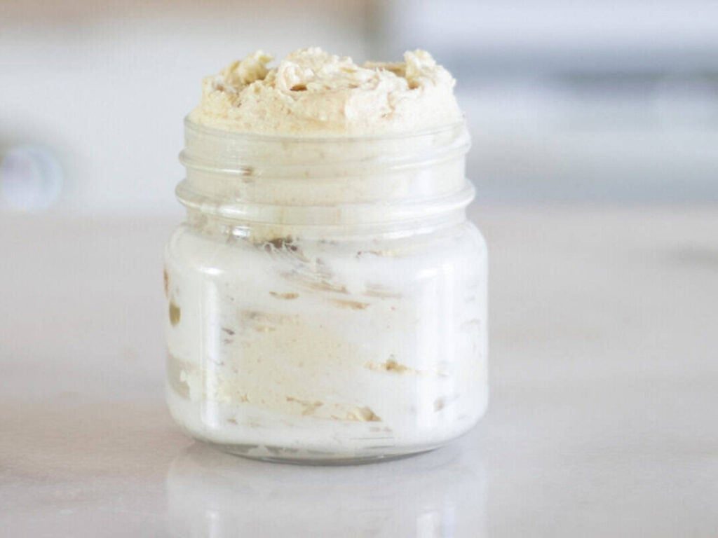 A glass jar of homemade body butter sitting on a kitchen counter.