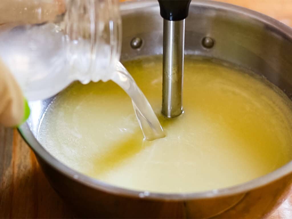 Pouring the lye water mixture into the bowl of oils and fats while blending with an immersion blender.