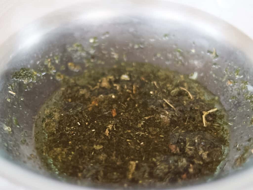 Herbs infusing in olive oil in a glass bowl.