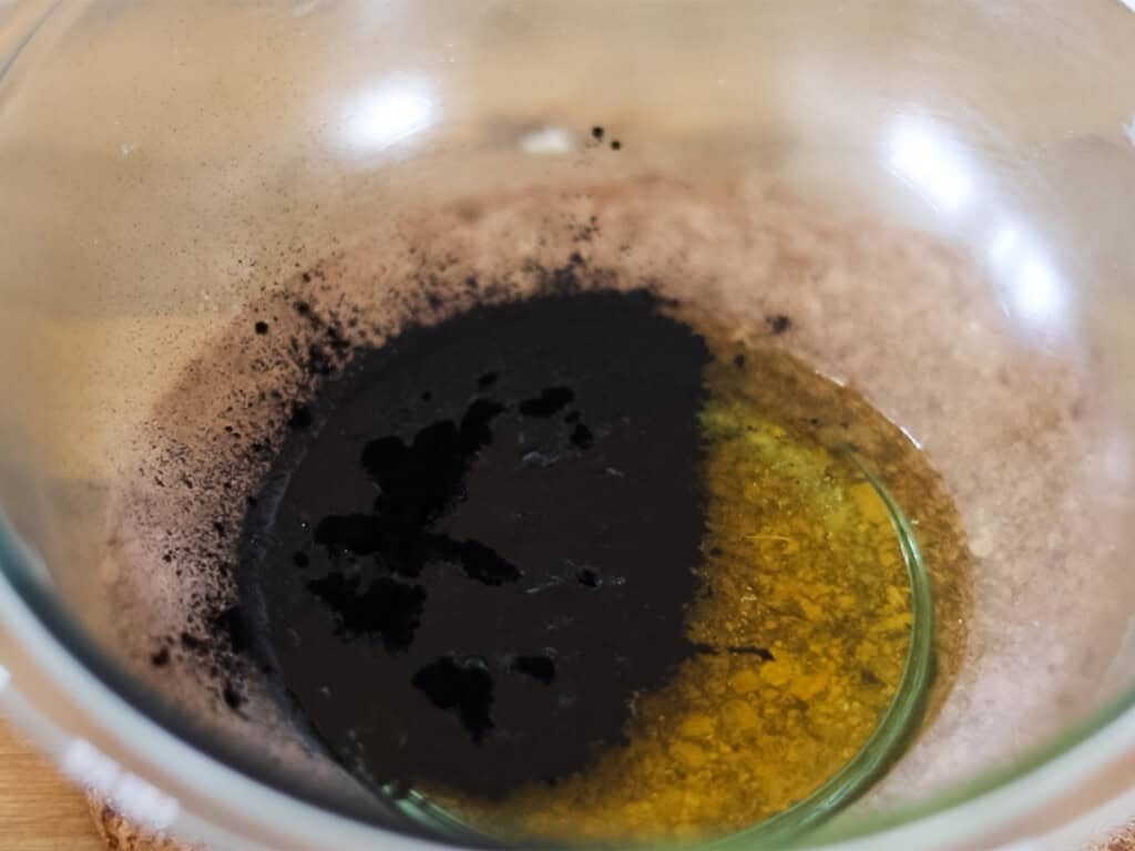 Activated charcoal sprinkled into a bowl of melted drawing salve ingredients.