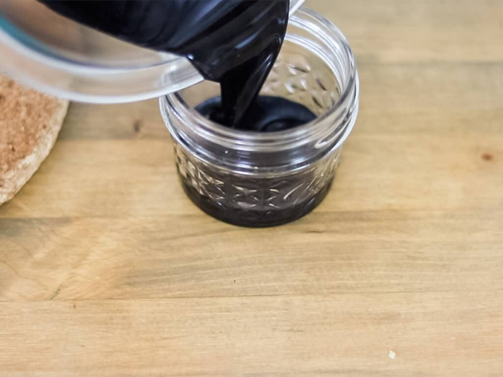 Pouring homemade drawing salve into a glass jar.