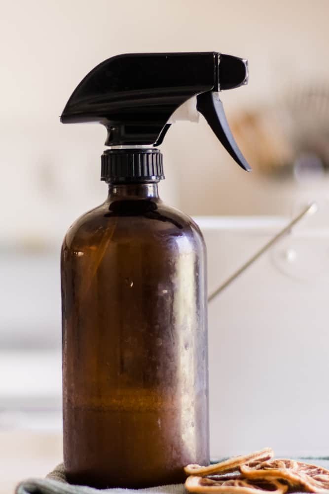 Large glass spray bottle with dusting solution on white marble table.