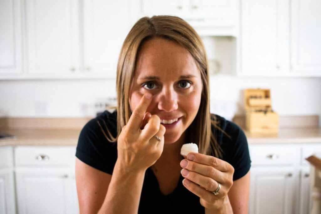 The author rubbing eye cream into her under-eyes while looking at the camera and smiling.