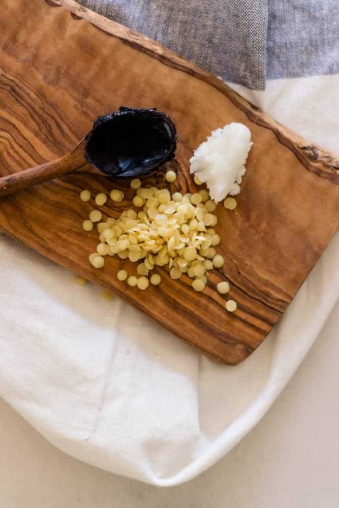 Activated charcoal, beeswax pellets, and coconut oil on wooden cutting board.