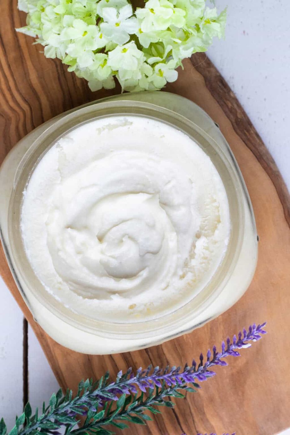 Homemade face moisturizer in a clear, wide mouth jar with lavender sprigs placed next to it.