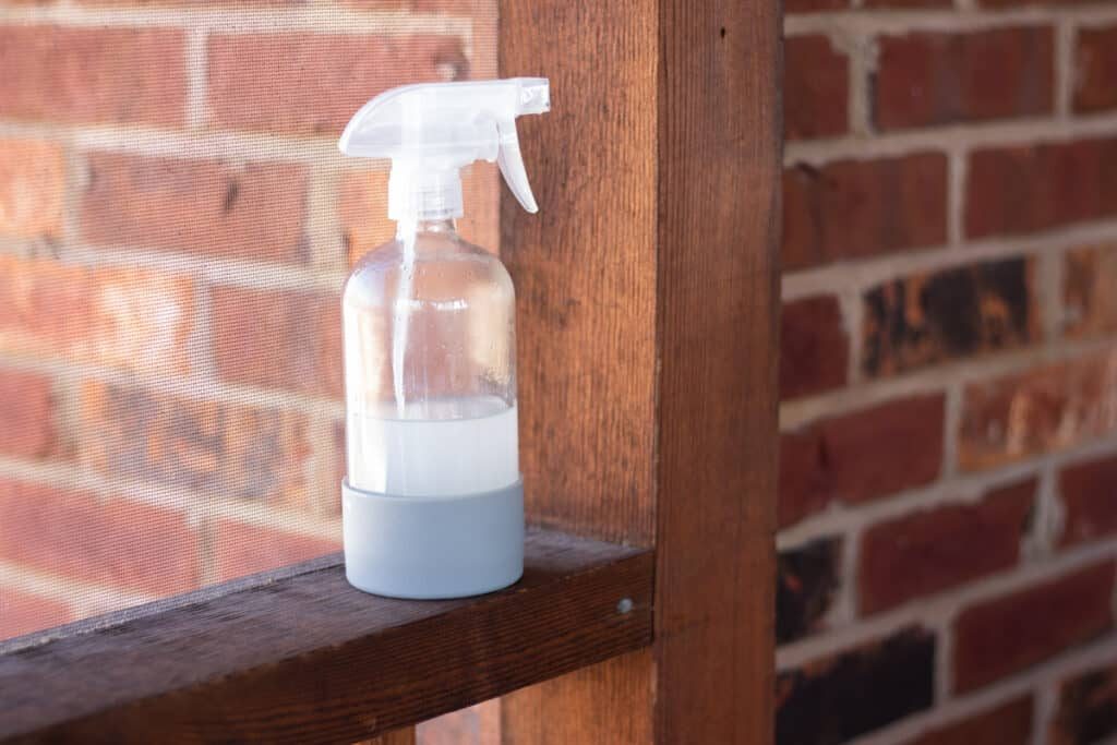 Our fly repellent recipe in a clear spray bottle with a blue rubber base on a wooden railing.