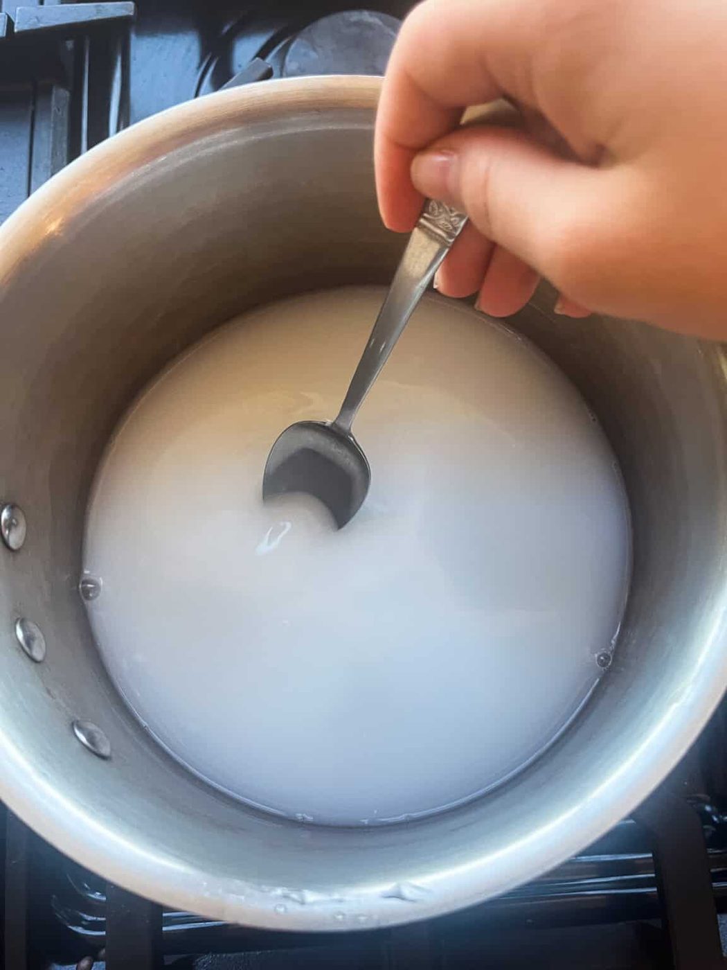 Stirring goat milk powder, water, and glycerin in a small saucepan.