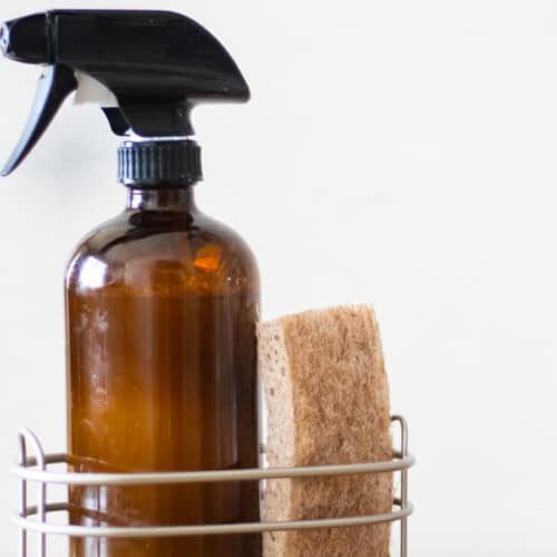 An amber bottle of homemade granite cleaner in a wire basket with a sponge.