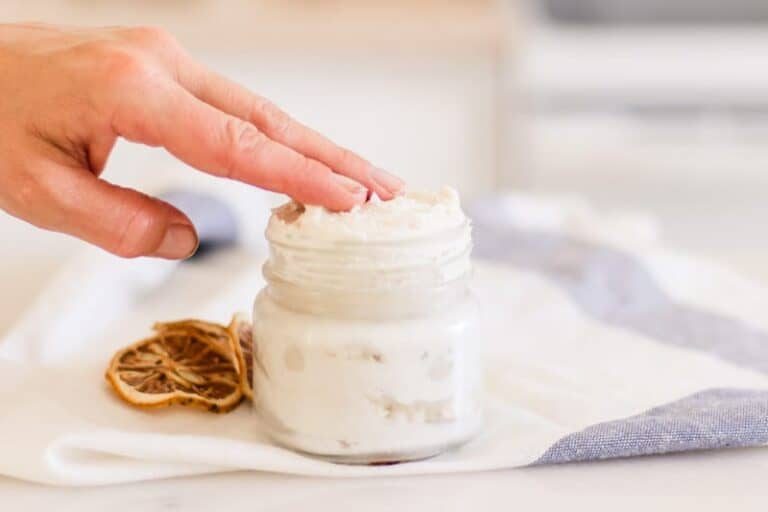 A small pot of moisturizing hand cream with a hand applying it.