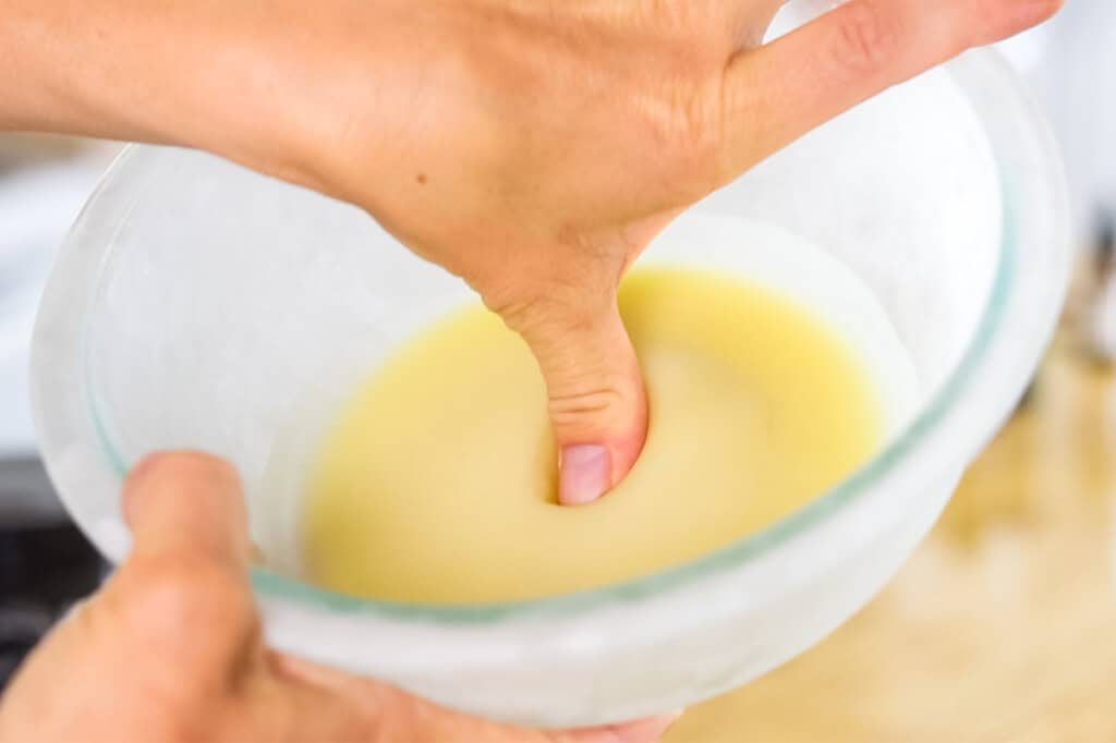 Pressing a thumb into the cream to test the firmness of it.