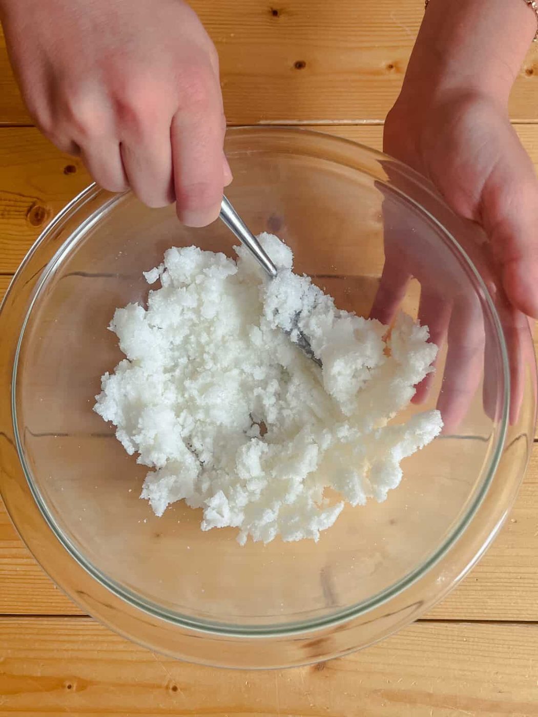 Stirring coconut oil and sugar together in a glass mixing bowl.