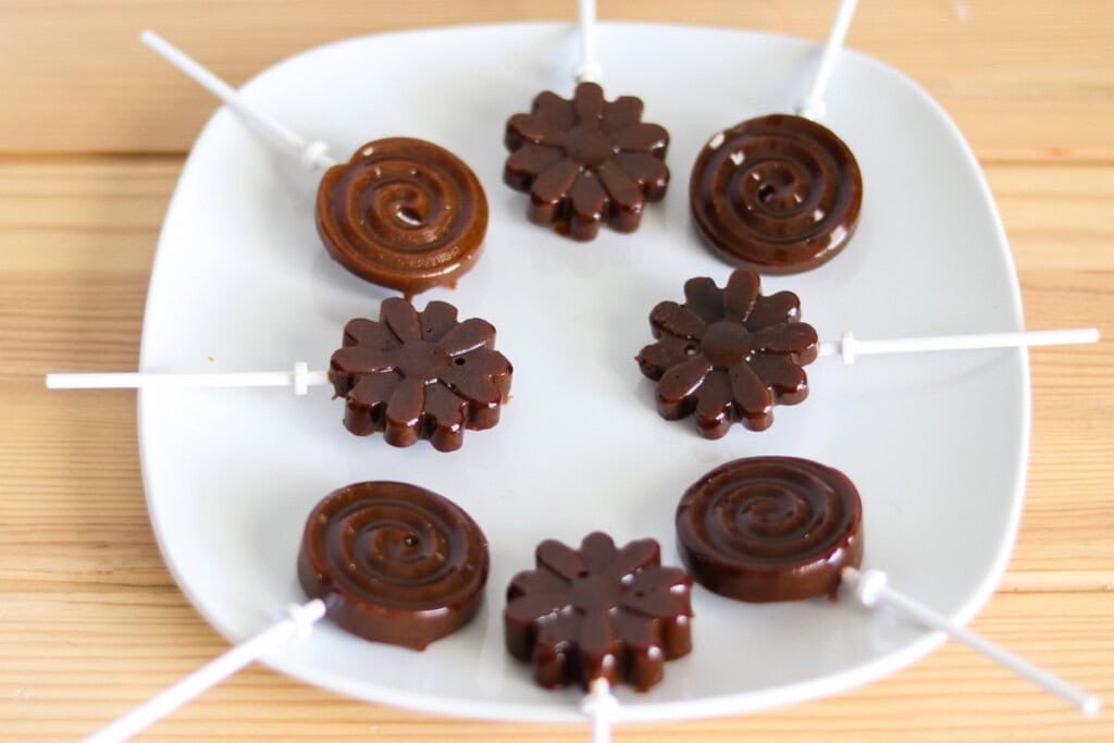 Homemade lollipops arranged on a white plate.