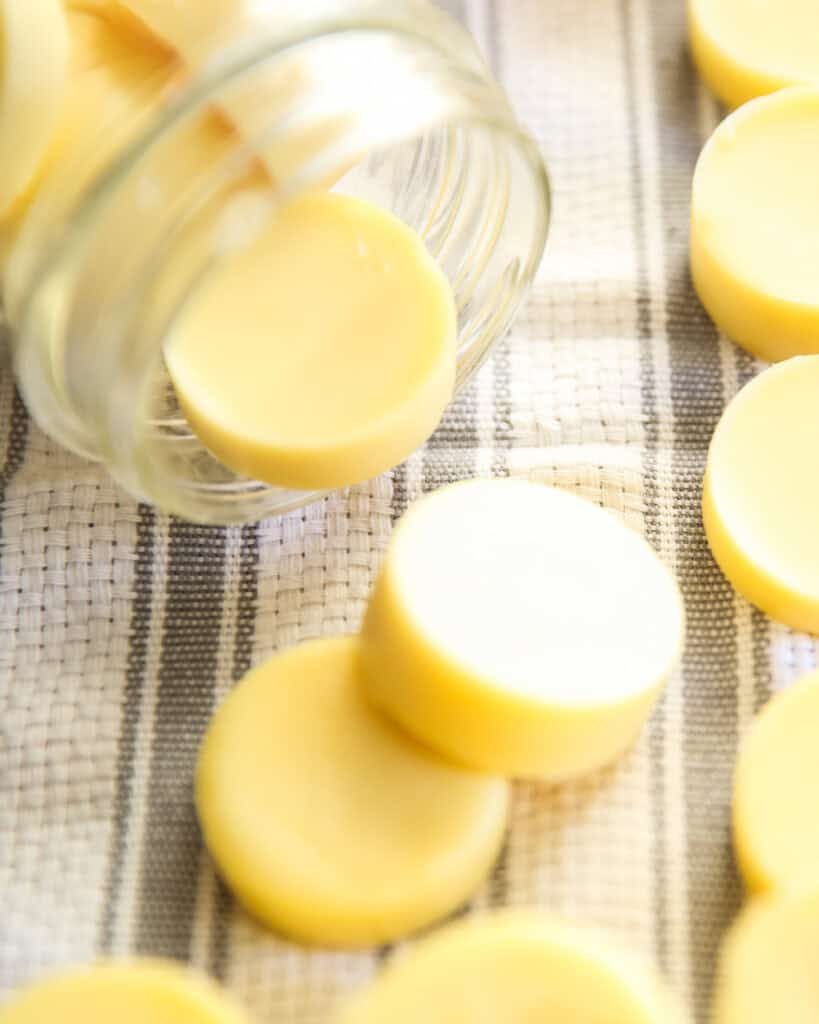 Homemade lotion bars spilled out of a large mouth mason jar onto a white and grey tea towel.