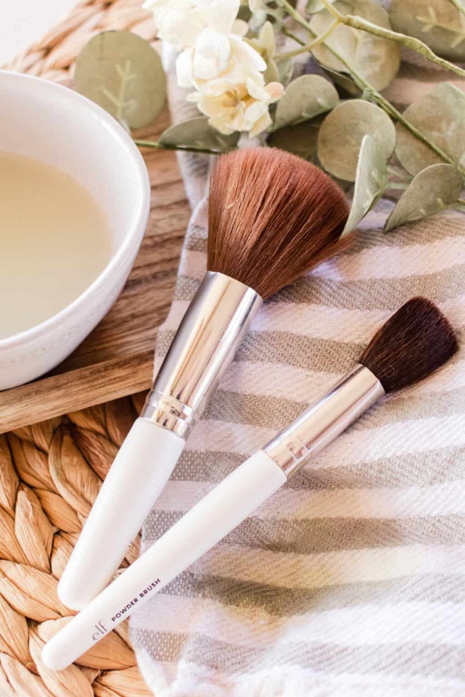 Makeup brushes with homemade makeup brush cleaner on a striped towel.