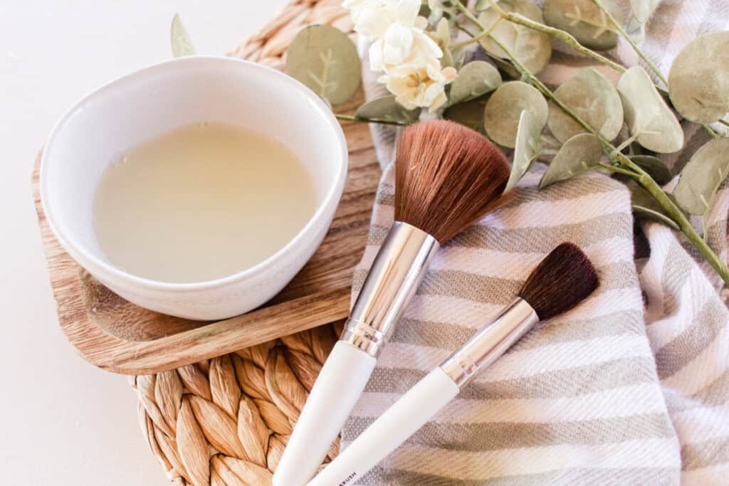 Makeup brushes on a towel with a bowl of makeup brush cleaner.