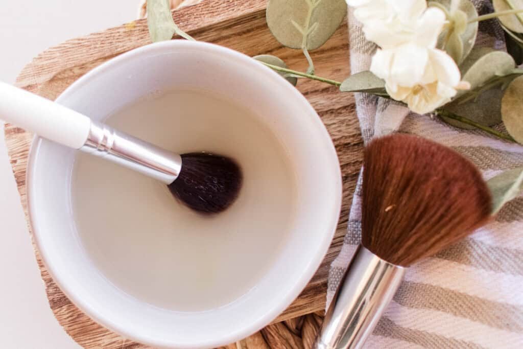 Swirling a makeup brush through a bowl of makeup brush cleaner.