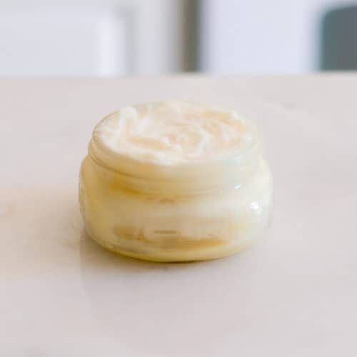 A jar of whipped mango body butter on a white counter.