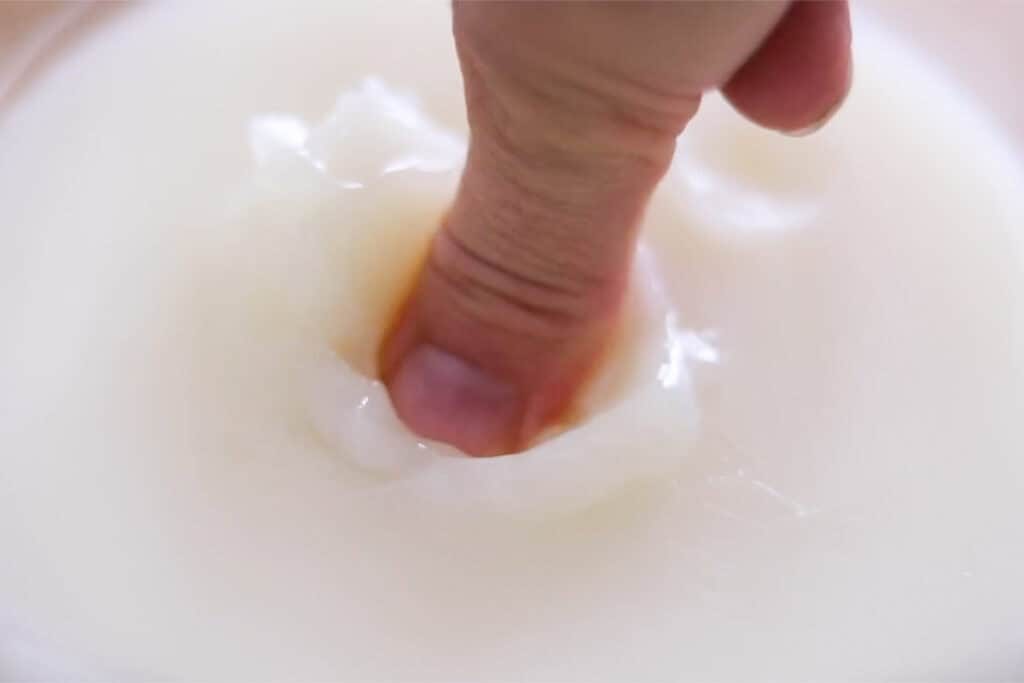 A finger making an indent in the frozen body butter. The mixture is firm but can easily be pressed into.
