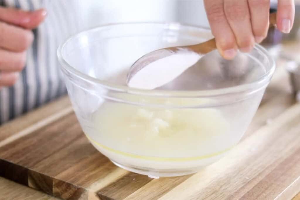 Adding arrowroot powder to the bowl with a wooden measuring spoon.