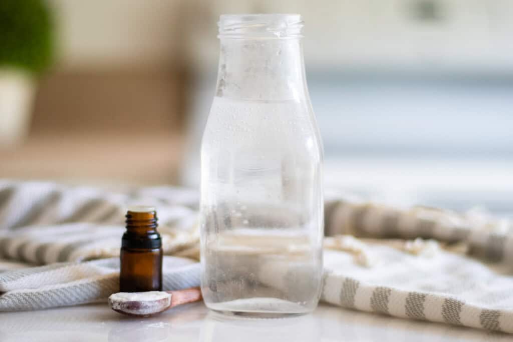 A jar of homemade mouthwash with a striped towel and a bottle of essential oil.