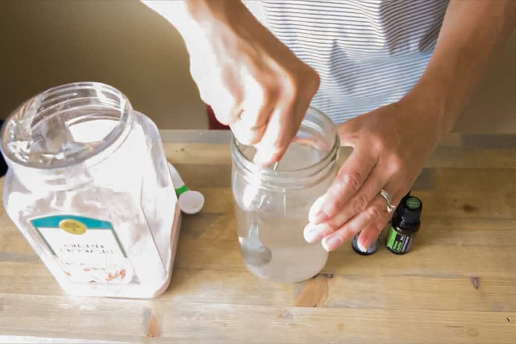 Stirring a glass jar of homemade mouthwash with a spoon.