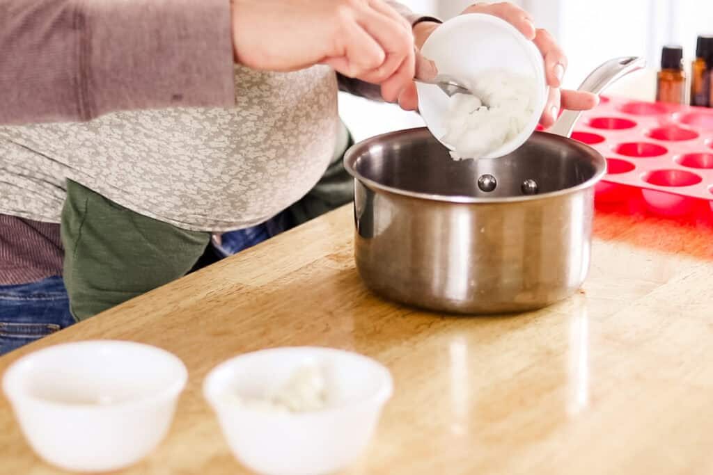 Pouring muscle rub ingredients into a suacepan.