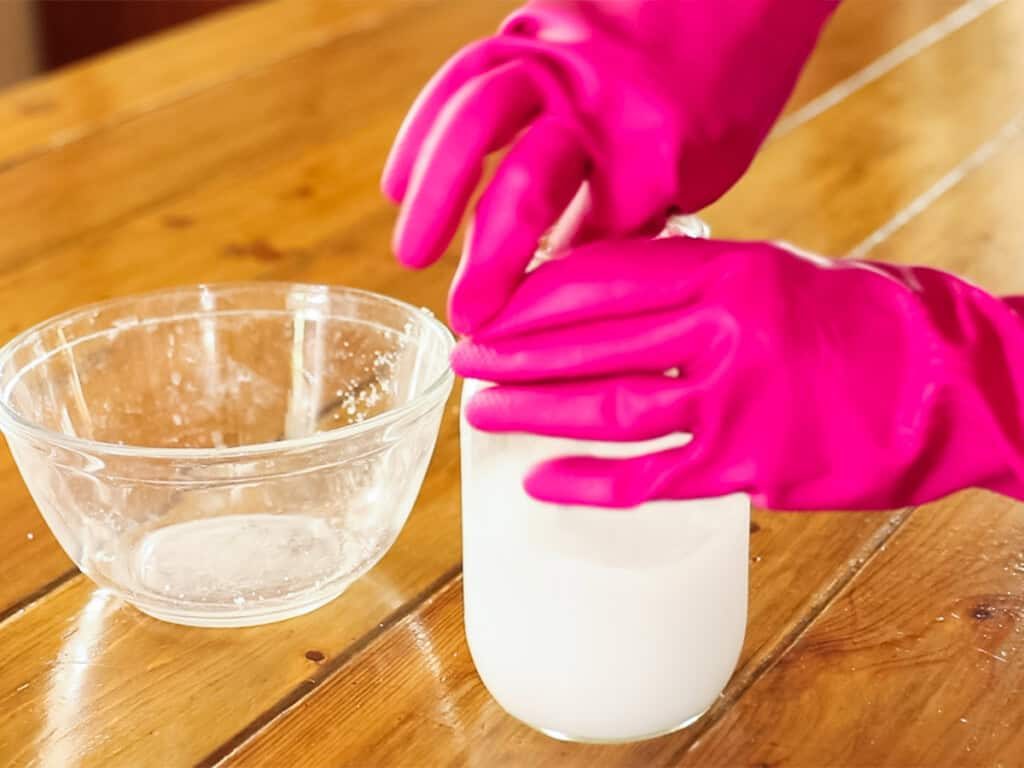 Stirring lye and water in a mason jar with rubber gloves on.
