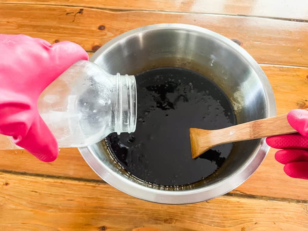 Pouring lye and water mixture into a bowl of oils and pine tar with a wooden spoon.