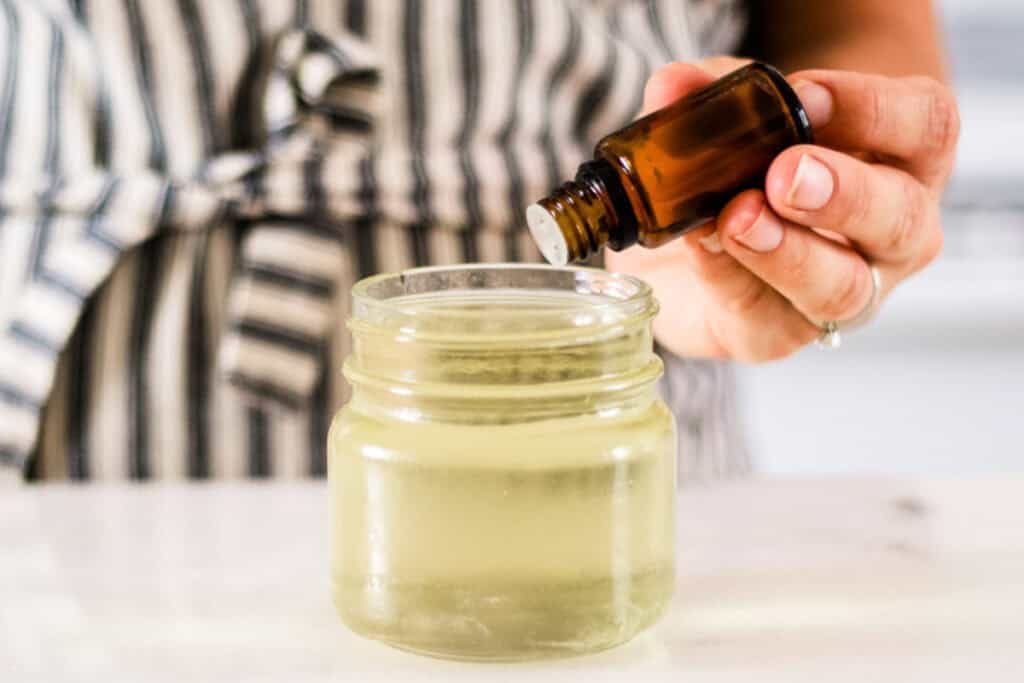 Adding essential oils to a jar of melted wax.