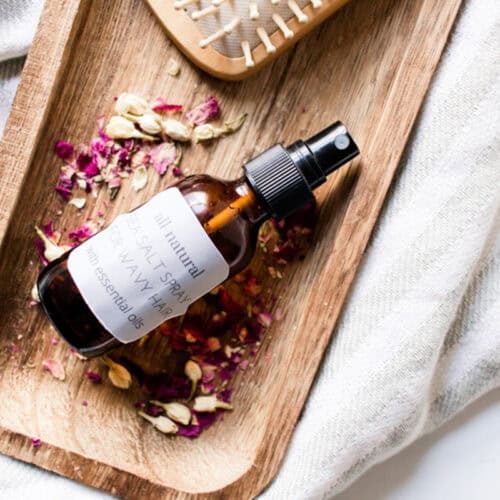 DIY sea salt spray on a wooden tray with a comb and rose petals.