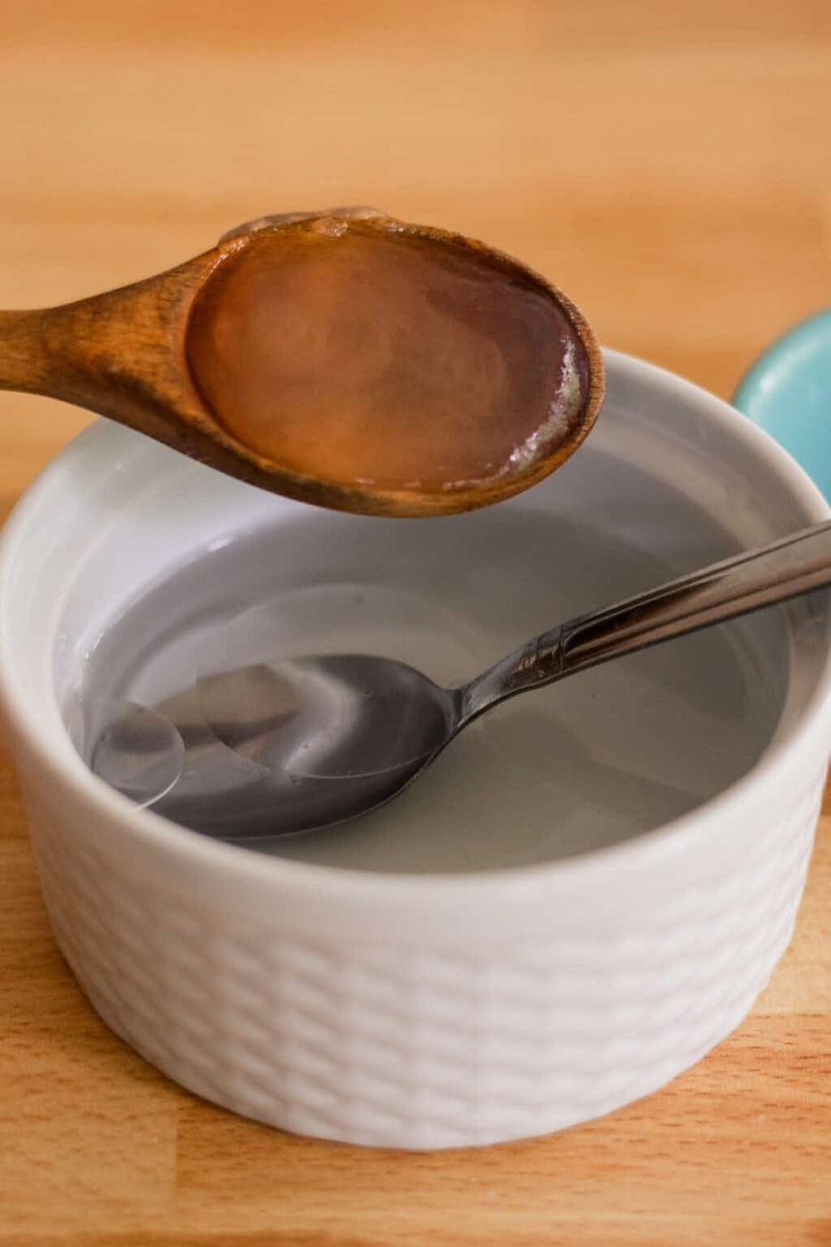 Pouring a wooden measuring spoon full of aloe vera into a small bowl to make sea salt spray.