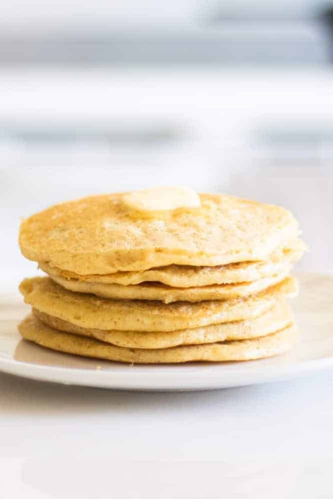 stack of sourdough pancakes on white plate with a chunk of butter
