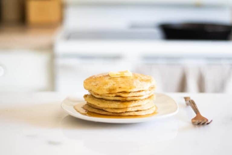 stack of pancakes on white marble counter with brass fork