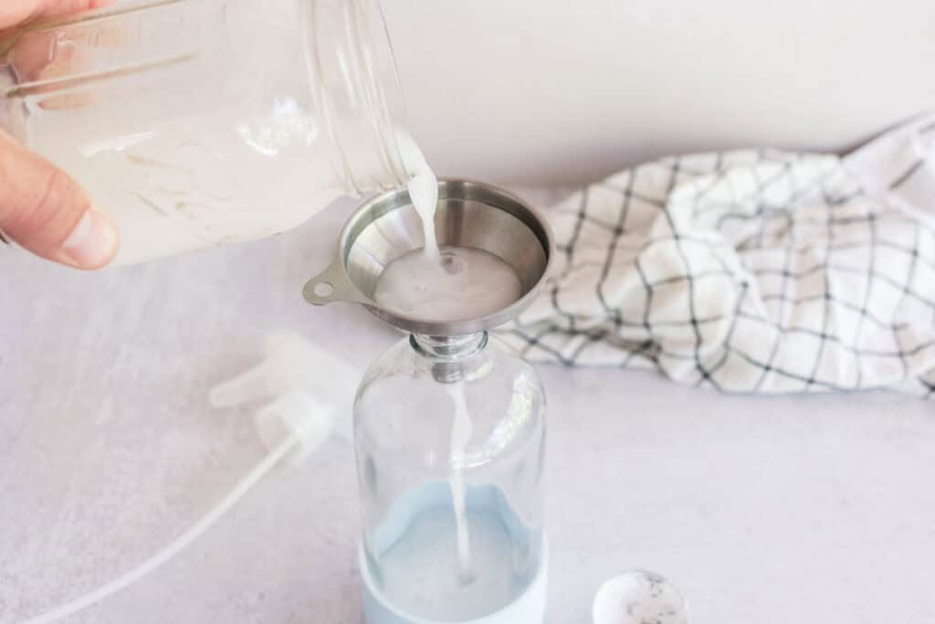 Pouring homemade spray starch into a spray bottle using a funnel.