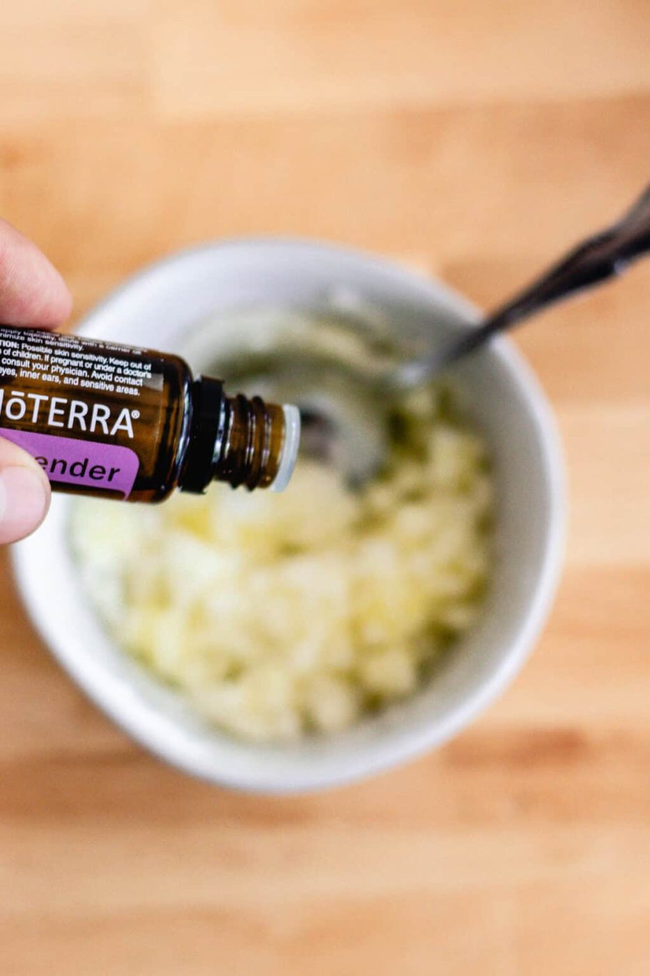 Dropping lavender essential oil into a bowl of mixed olive oil and sugar.