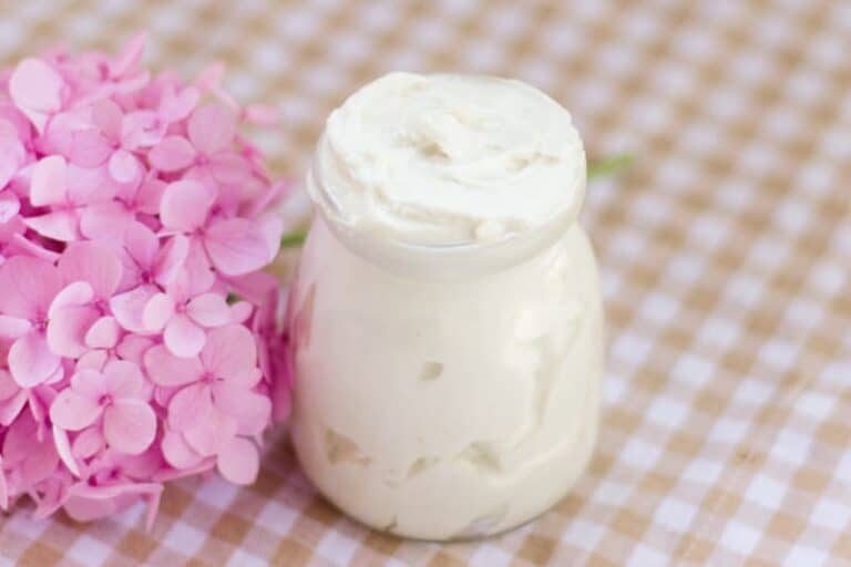 A small jar of tallow butter with pink flowers next to it on a checked table cloth.