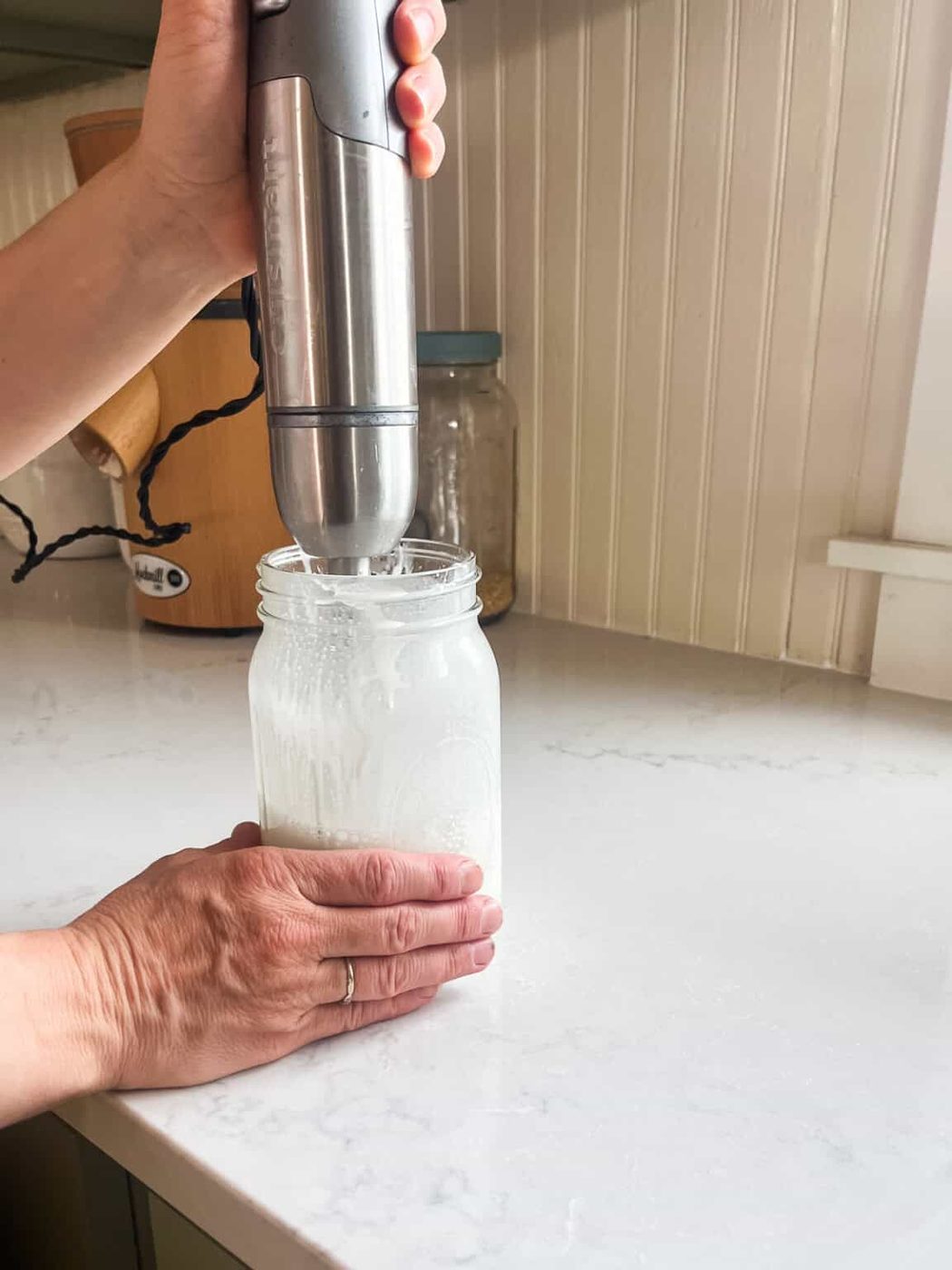Blending a jar of homemade tallow lotion with an immersion blender.