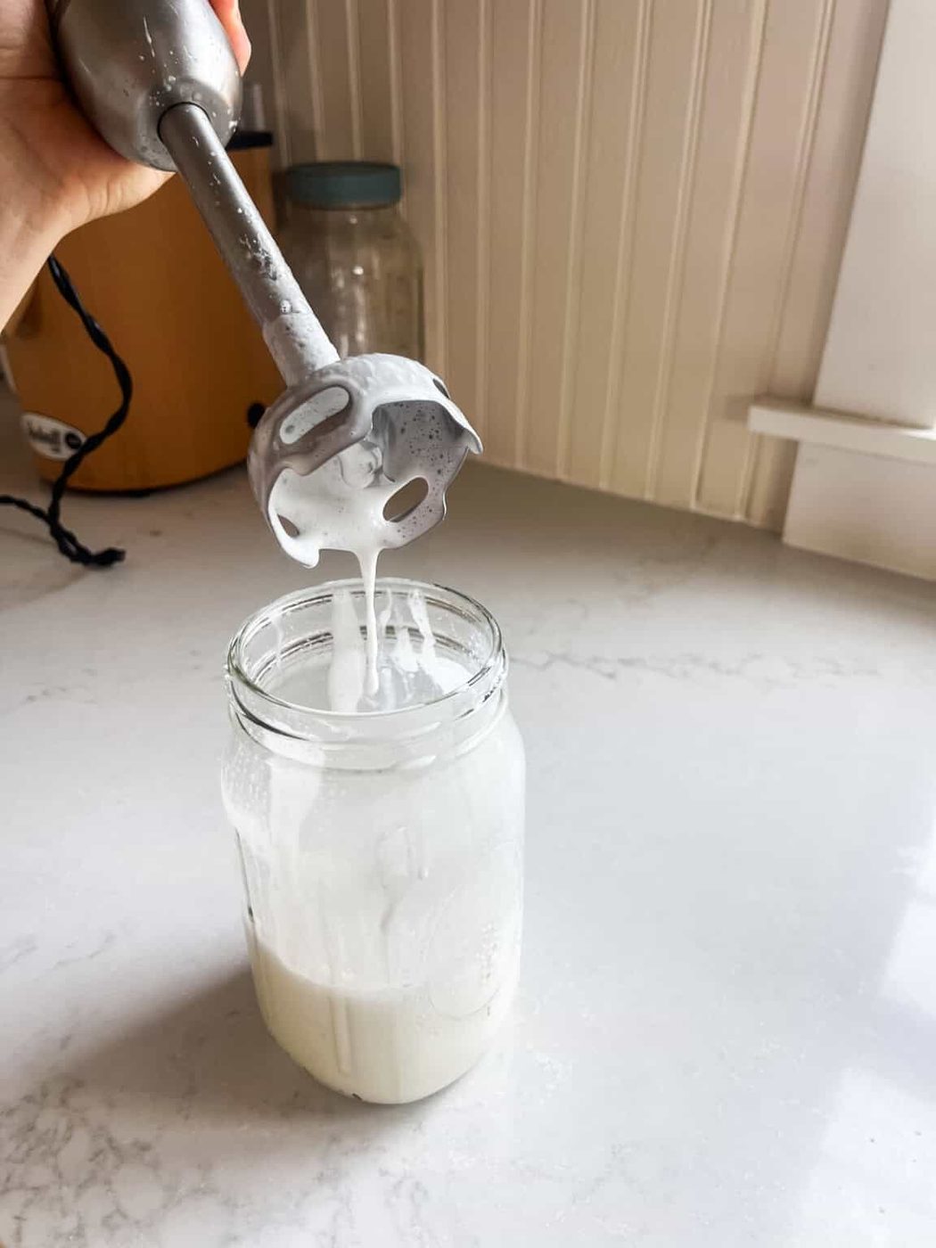 Lifting an immersion blender out of a jar of homemade tallow lotion.